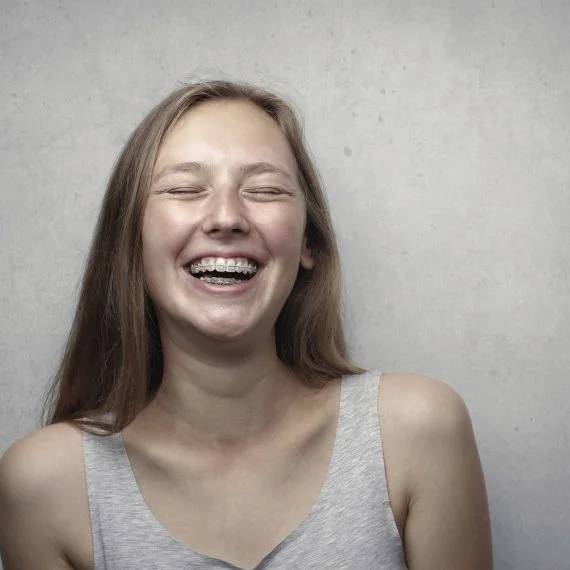 Young woman smiling broadly with her eyes closed, displaying a bright, confident smile with visible white teeth